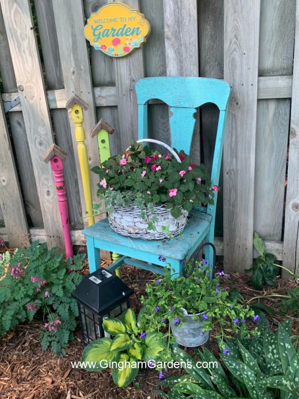 Image of an old chair, faux birdhouse stakes and a sign in a garden.