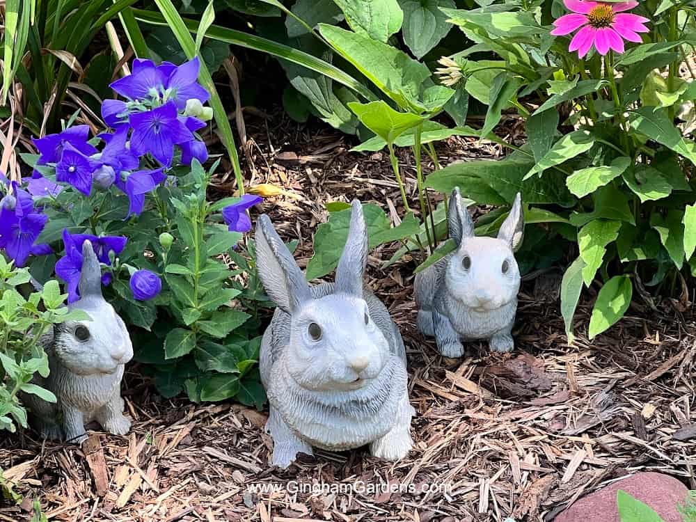 Mom and two baby bunny statues in a flower garden.