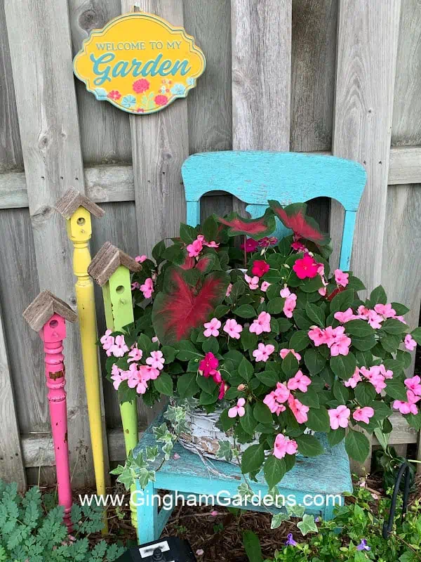 Cute garden grouping with an old chair, faux birdhouse stakes and a welcome sign on an old fence.