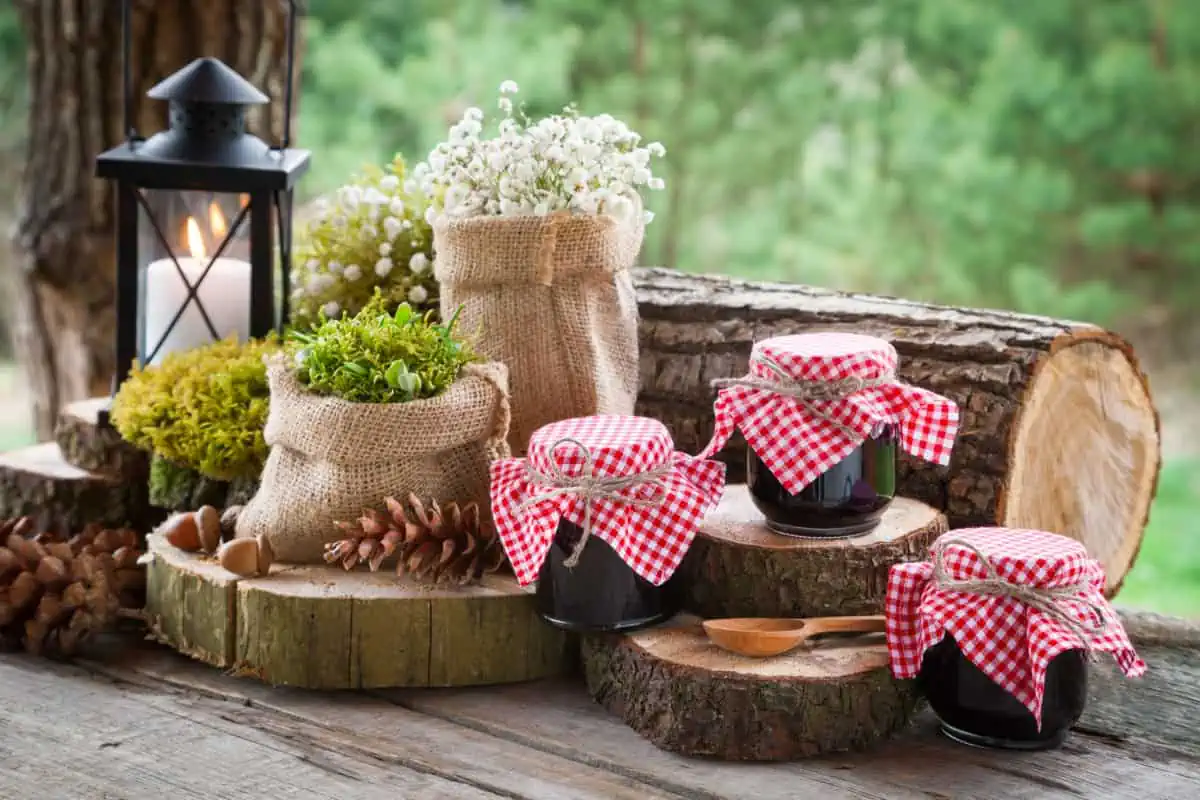 Rustic photo with burlap bags of herbs and flowers and jars of jellies with gingham covers arranged on log slices. Gifts from Your Garden