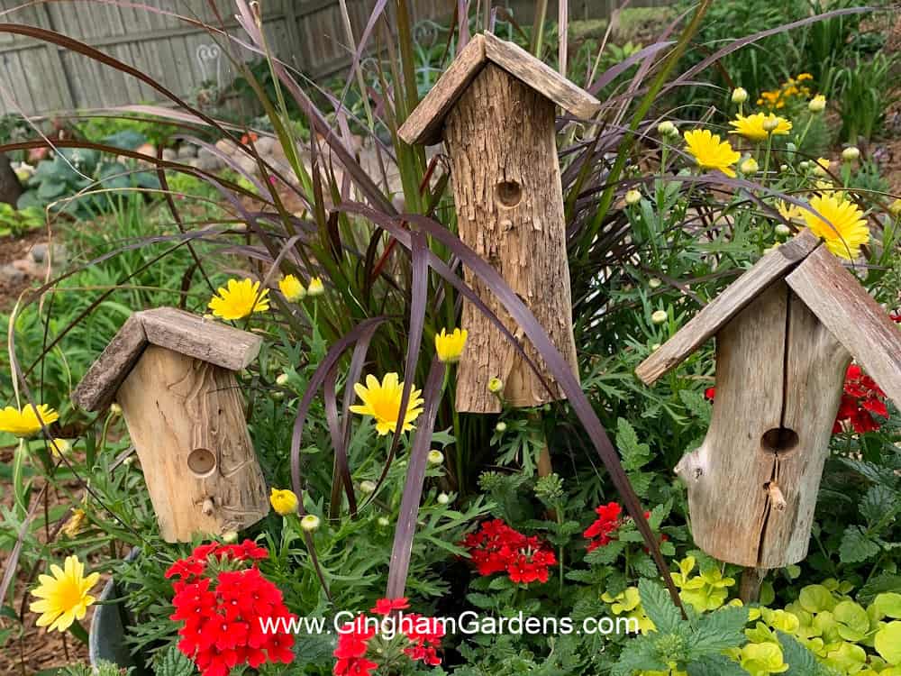 3 decorative faux birdhouse garden stakes made from tree branches displayed in a planter.