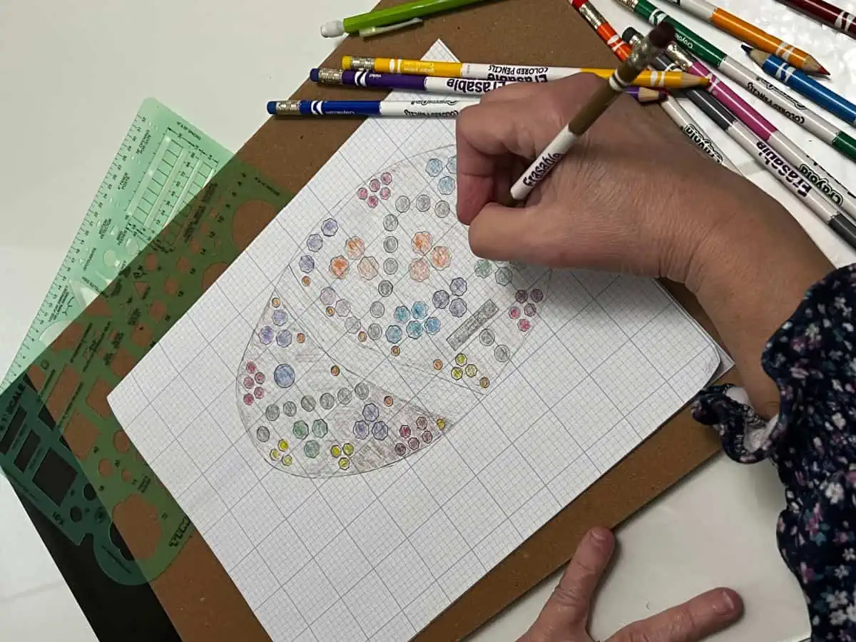 Drawing of a garden plan with gardener's hand holding a colored pencil.